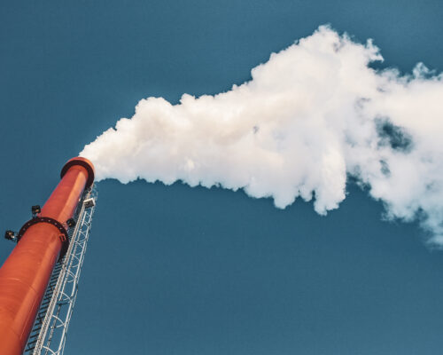 Skorsten med rök på en klarblå himmel från ett fjärrvärmeverk.